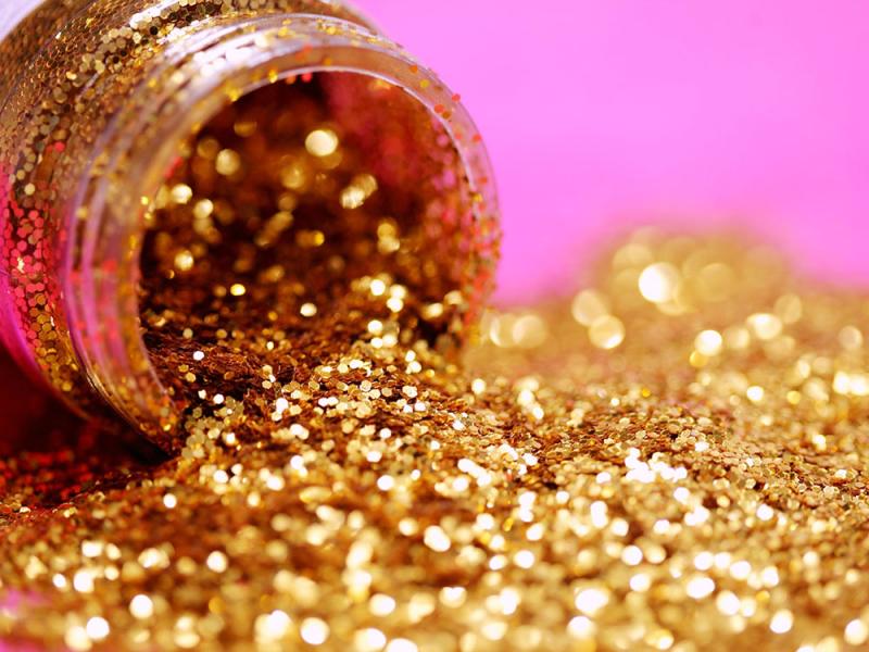 Gold glitter spilling out of bootle on pink background