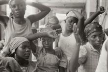 Group of women stading close togetehr, some with fists raised and wearing scarves on their heads.